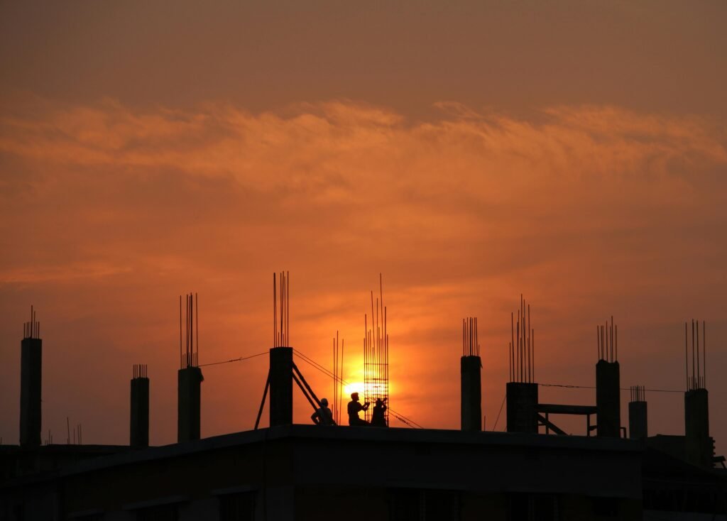 Yeso y pladur en Tenerife Silhouette of workers on a construction site against a vibrant sunset sky.